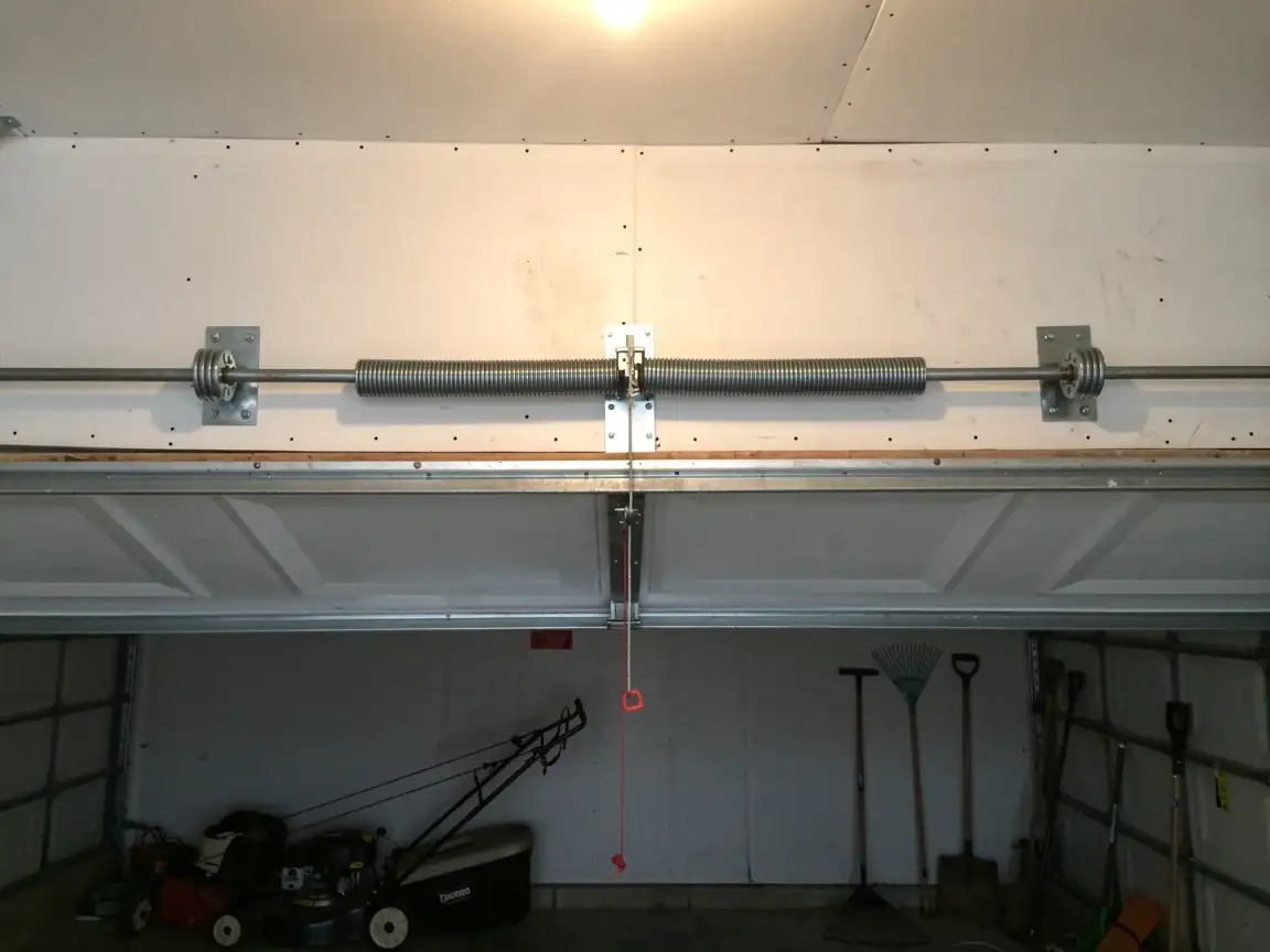 A torsion spring is mounted above a partially open garage door.